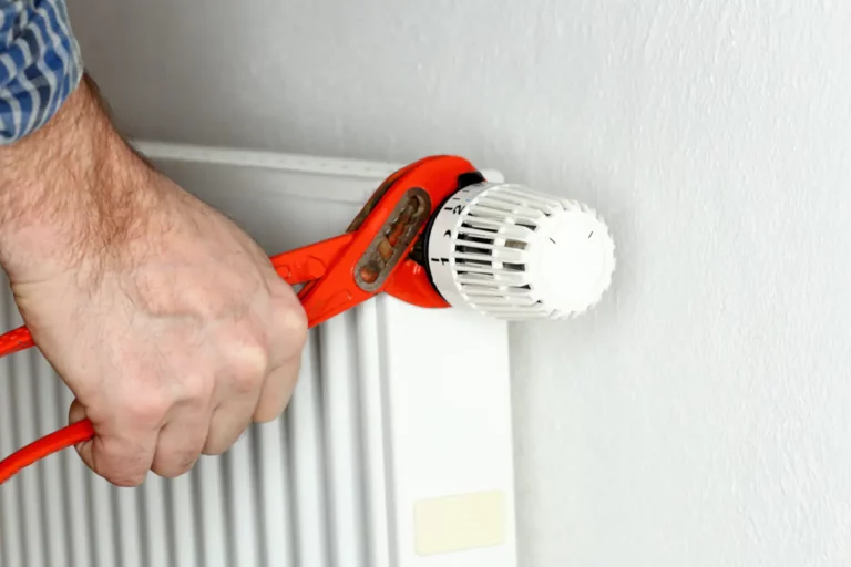 Eine Hand hält Rohrzange am Thermostat eines Heizkörpers